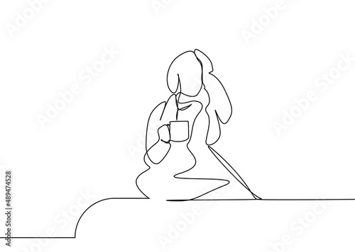 a woman with a headache is drinking coffee and herbal tea in her hand in a blanket at home
