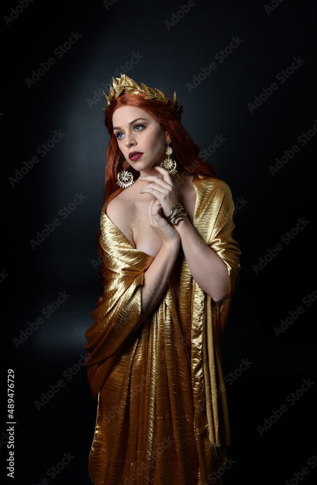Full length portrait of pretty female model wearing grecian goddess toga gown, posing with elegant gestural movements on a studio background. Full length portrait of pretty female model wearing grecian goddess toga gown, posing with elegant gestural movements on a studio background.