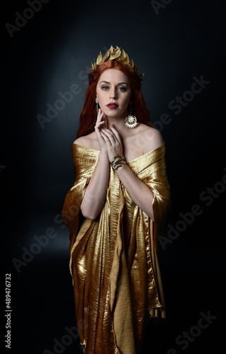 Fototapeta Full length portrait of pretty female model wearing  grecian goddess  toga gown, posing with elegant gestural movements on a studio background