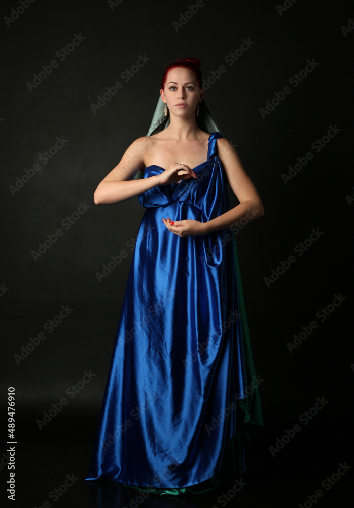 Full length portrait of pretty female model wearing grecian goddess toga gown, posing with elegant gestural movements on a studio background. Full length portrait of pretty female model wearing grecian goddess toga gown, posing with elegant gestural movements on a studio background.