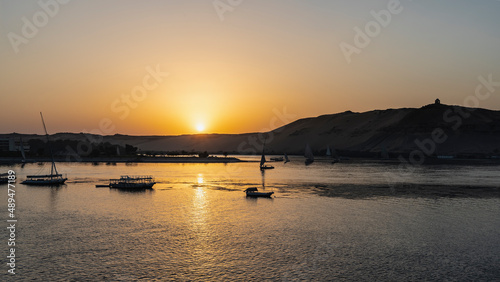 A calm sunset on the Nile. The sun is low over the sand dunes. The sky is highlighted in orange. A sunny path on the water. Tourist boats on the river. Egypt. Aswan