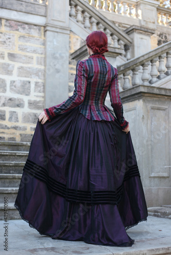 Full length portrait of red-haired woman wearing a historical victorian gown costume, walking around beautiful location with Gothic stone architecture.
