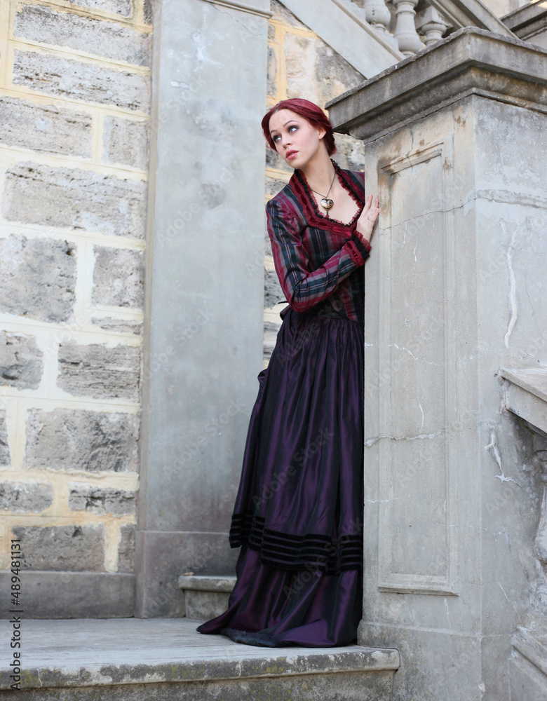 Full length portrait of red-haired woman wearing a historical victorian gown costume, walking around beautiful location with  Gothic stone architecture.
