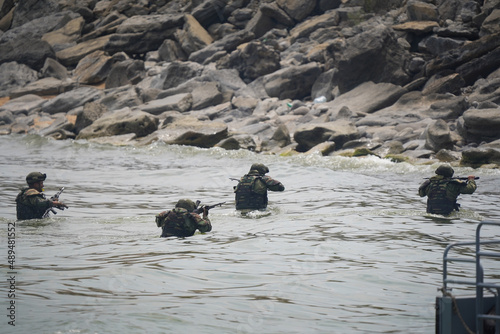 Four soldiers in military uniforms come out of the water to the shore with a rifle over their heads. War games or military exercises.  © Danila Shtantsov
