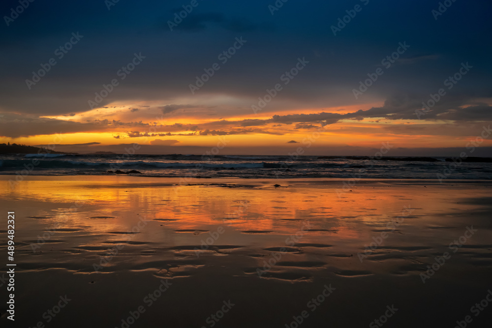 Scenic sunset on the ocean sandy beach with town silhouette on the horizon. Beautiful view landscape travel background. foorptints on sand.