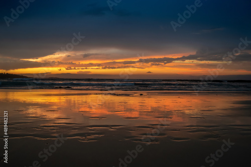 Scenic sunset on the ocean sandy beach with town silhouette on the horizon. Beautiful view landscape travel background. foorptints on sand. © Daria Nipot