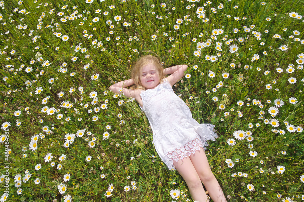 Cute little girl lie in big camomile meadow