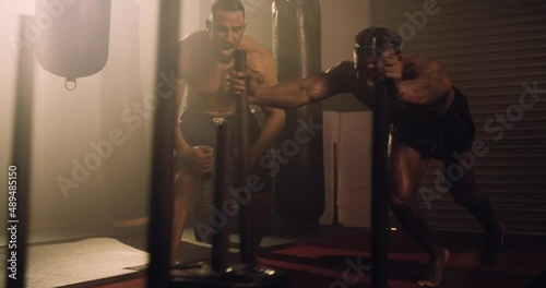 An African American and Hispanic Athlete Sled Sprint Training In A Gym. Shot In An MMA Boxing Gym With Low Key Lighting And A Scattering Of Haze. Captured On Red Digital Cinema Camera 