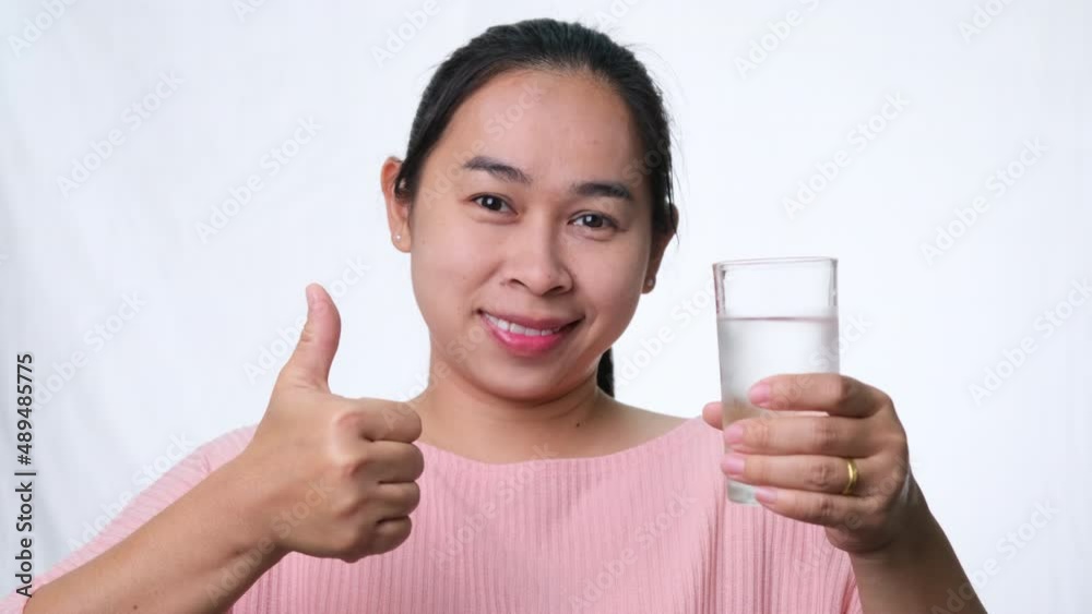 Smiling woman holding a glass of water and thumbs up on white background in studio. Healthy lifestyle Smiling woman holding a glass of water and thumbs up on white background in studio. Healthy lifestyle