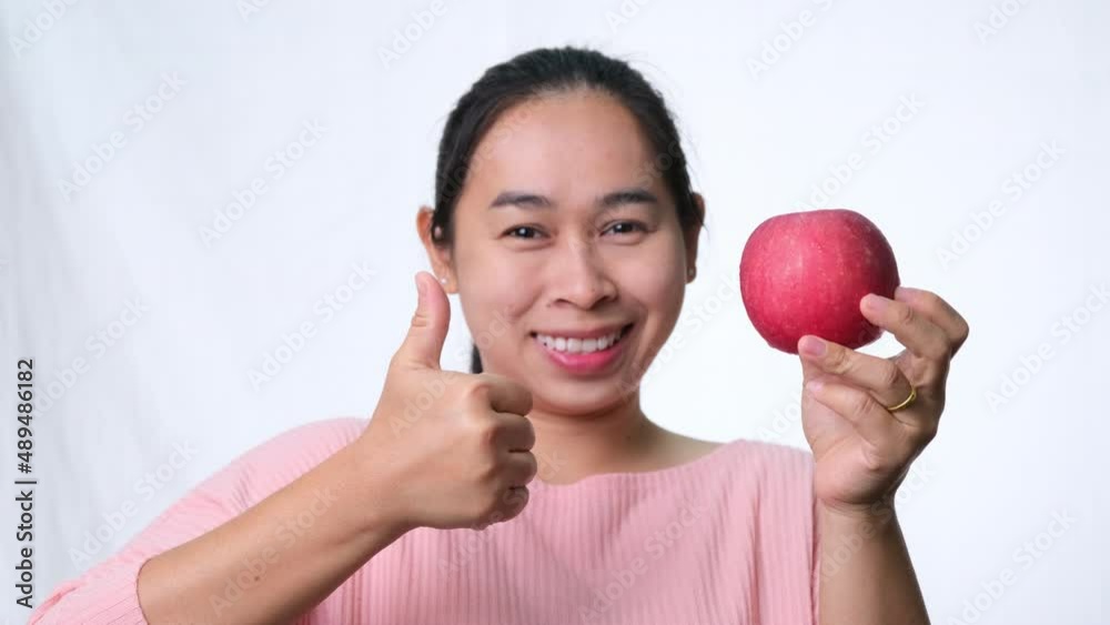 Asian woman holding red apple with thumbs up and smiling showing healthy teeth on white background in studio Asian woman holding red apple with thumbs up and smiling showing healthy teeth on white background in studio