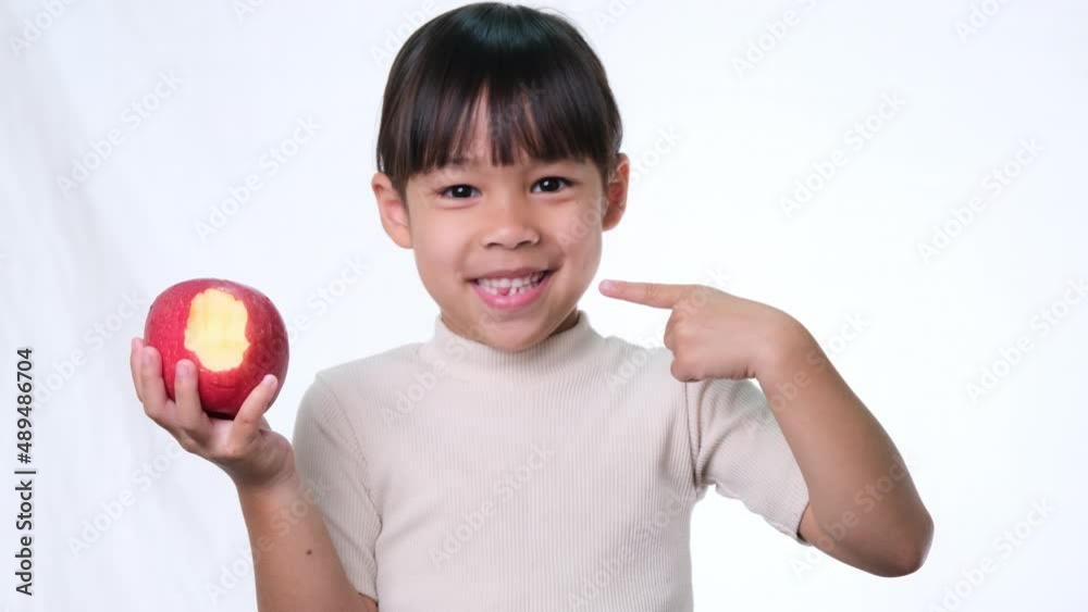 Happy little girl with apple. Cute Asian little girl eating organic apple on white background in studio. Healthy nutrition for small children. Happy little girl with apple. Cute Asian little girl eating organic apple on white background in studio. Healthy nutrition for small children.