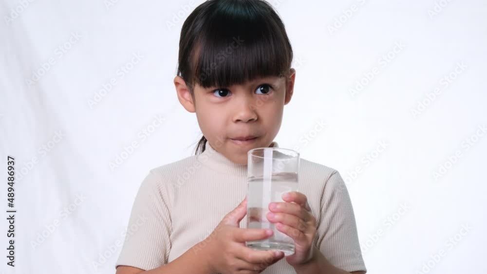 Cute little asian girl drinking water from a glass on white background in studio. Good healthy habit for children. Healthcare concept Cute little asian girl drinking water from a glass on white background in studio. Good healthy habit for children. Healthcare concept