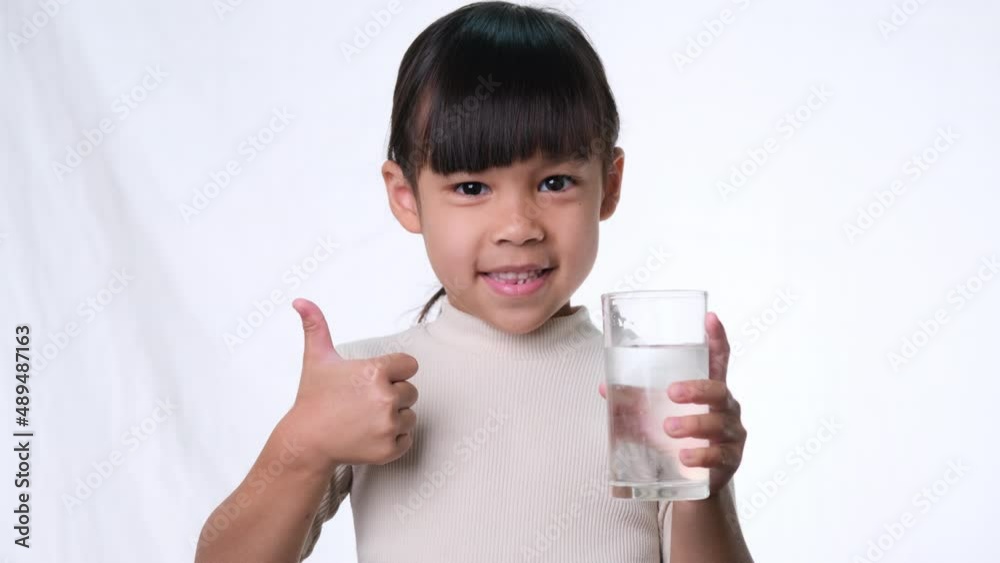 Cute little asian girl holding a glass of water and showing thumbs up on white background in studio. Good healthy habit for children. Healthcare concept Cute little asian girl holding a glass of water and showing thumbs up on white background in studio. Good healthy habit for children. Healthcare concept