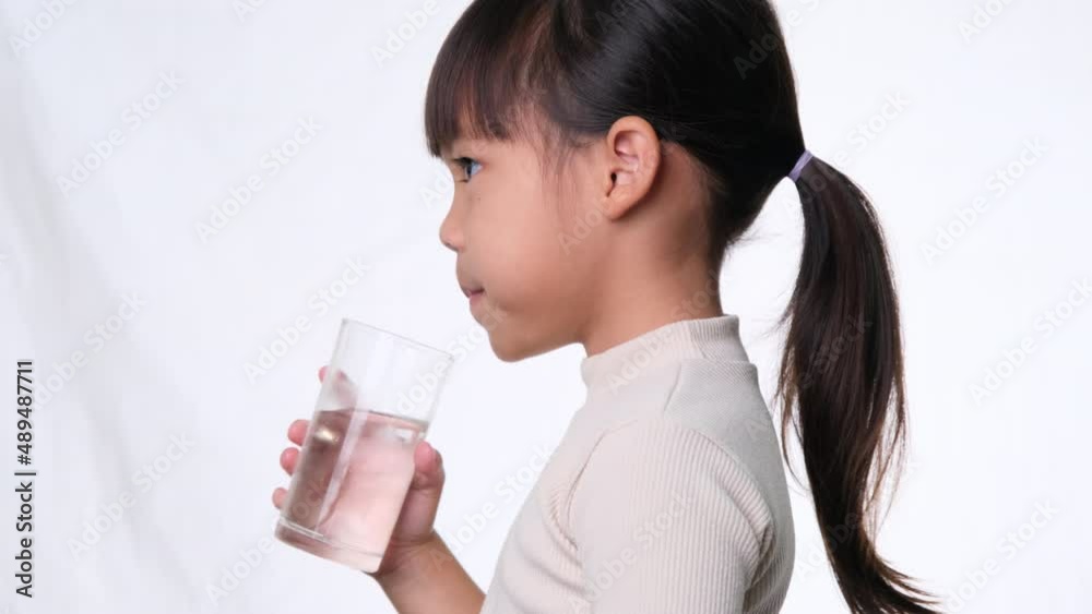 Cute little asian girl drinking water from a glass on white background in studio. Good healthy habit for children. Healthcare concept Cute little asian girl drinking water from a glass on white background in studio. Good healthy habit for children. Healthcare concept