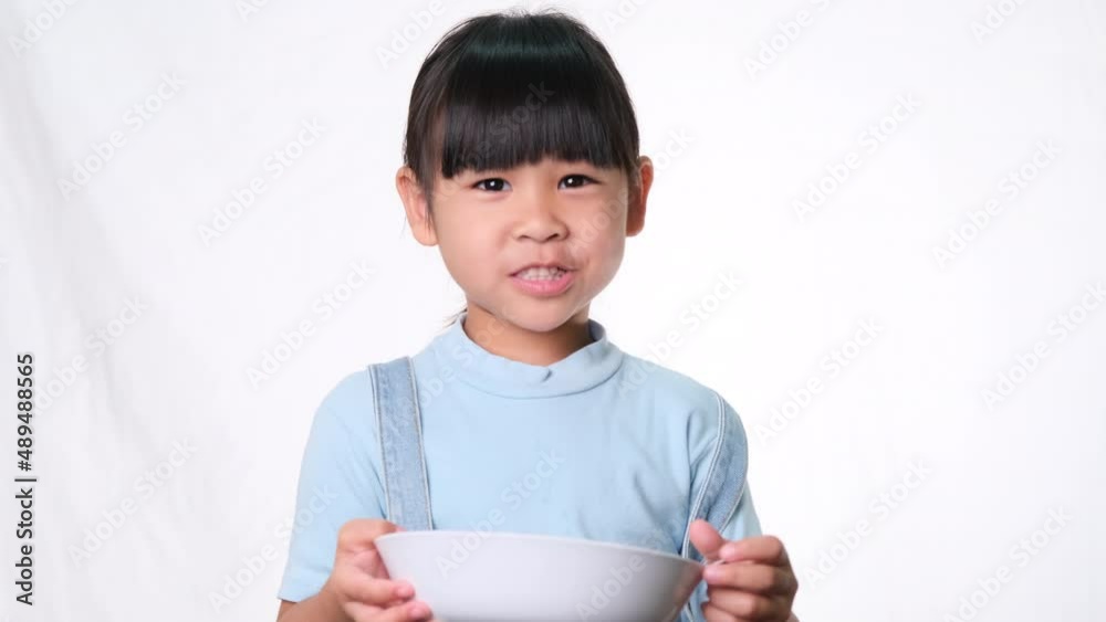 Cute little girl having breakfast. Happy little girl eating cereal with milk from bowl on white background in studio. Healthy nutrition for children. Cute little girl having breakfast. Happy little girl eating cereal with milk from bowl on white background in studio. Healthy nutrition for children.