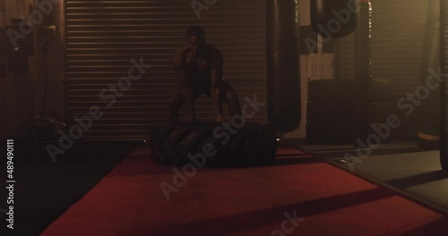 An African American Athlete Exercises, Tyre Flipping In A Crossfit Gym. Shot In An MMA Boxing Gym With Low Key Lighting And A Scattering Of Haze. Captured On Red Digital Cinema Camera 