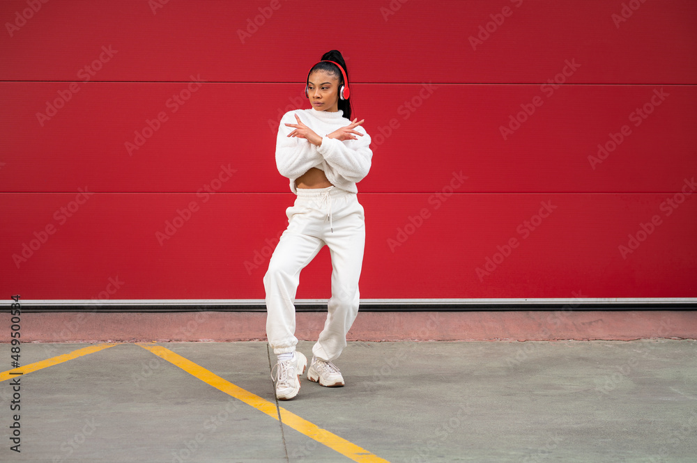Cheerful African American woman with headphones
dancing urban dance on a red background
