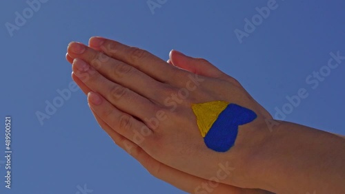 female praying hands painted in Ukraine flag colors yellow-blue against blue sky. Pray for Ukraine photo