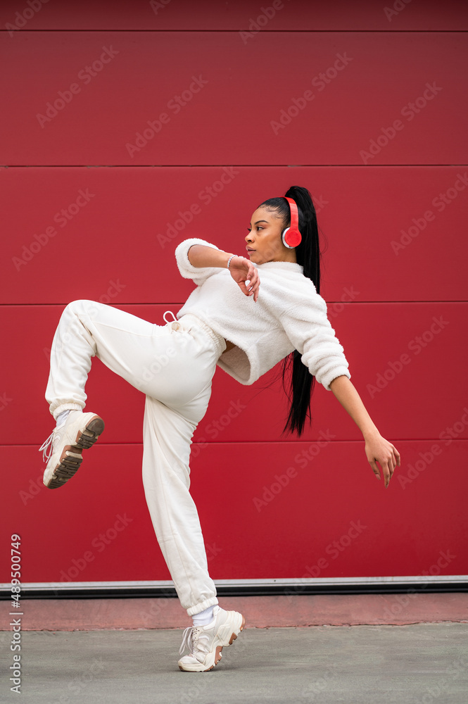 Cheerful African American woman with headphones
dancing urban dance on a red background