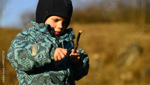 Little boy using a real sharp knife to sharpen a wooden stick. Real life play with real tool. Kid uses real tool. Raising children. Hard light and shadows.