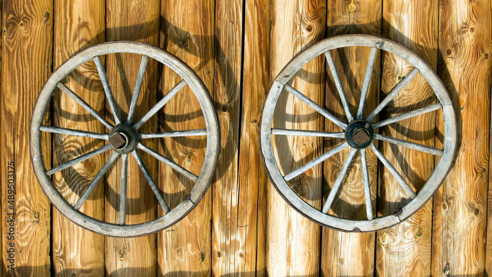Two old wooden wheels on a log background, interior decor Two old wooden wheels on a log background, interior decor