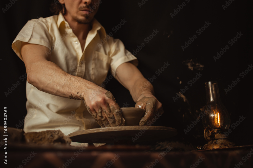 man in pottery workshop makes plate of clay, an authentic atmosphere, yellow lamp, lifestyle, magical atmosphere. Concept with your own hands, home entertainment. potter's wheel man in pottery workshop makes plate of clay, an authentic atmosphere, yellow lamp, lifestyle, magical atmosphere. Concept with your own hands, home entertainment. potter's wheel