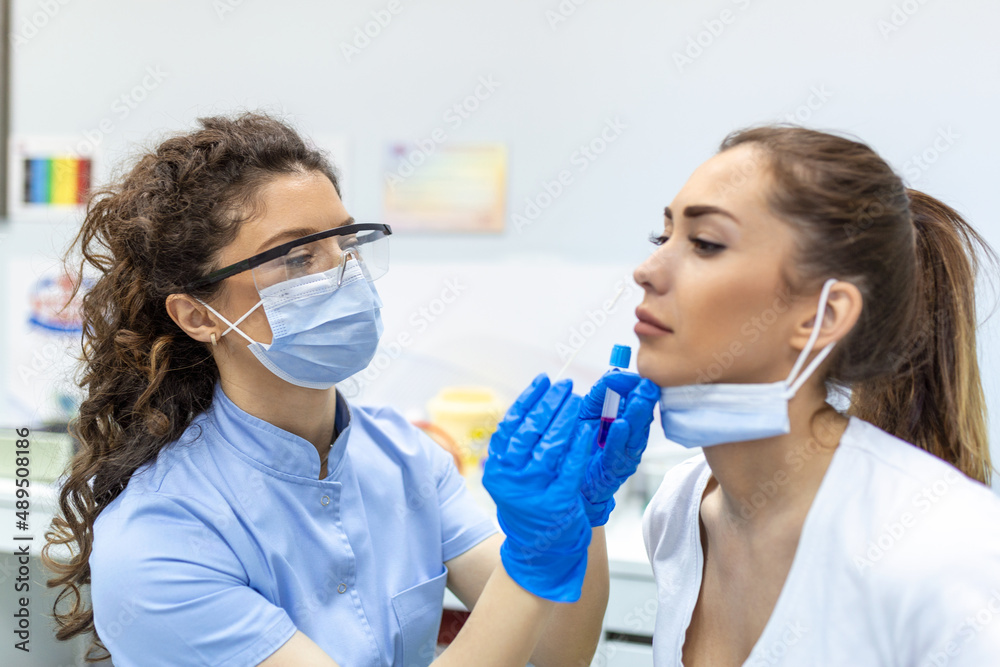 Female patient wearing mask is having sample taken from nose for a pcr test for Covid 19. Healthcare worker with protective equipment performs coronavirus swab on woman. Nose swab for Covid-19. Female patient wearing mask is having sample taken from nose for a pcr test for Covid 19. Healthcare worker with protective equipment performs coronavirus swab on woman. Nose swab for Covid-19.