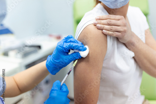 Practitioner vaccinating woman patient in clinic. Doctor giving injection to woman at hospital. Nurse holding syringe and inject Covid-19 or coronavirus vaccine.Injection covid vaccine concept.