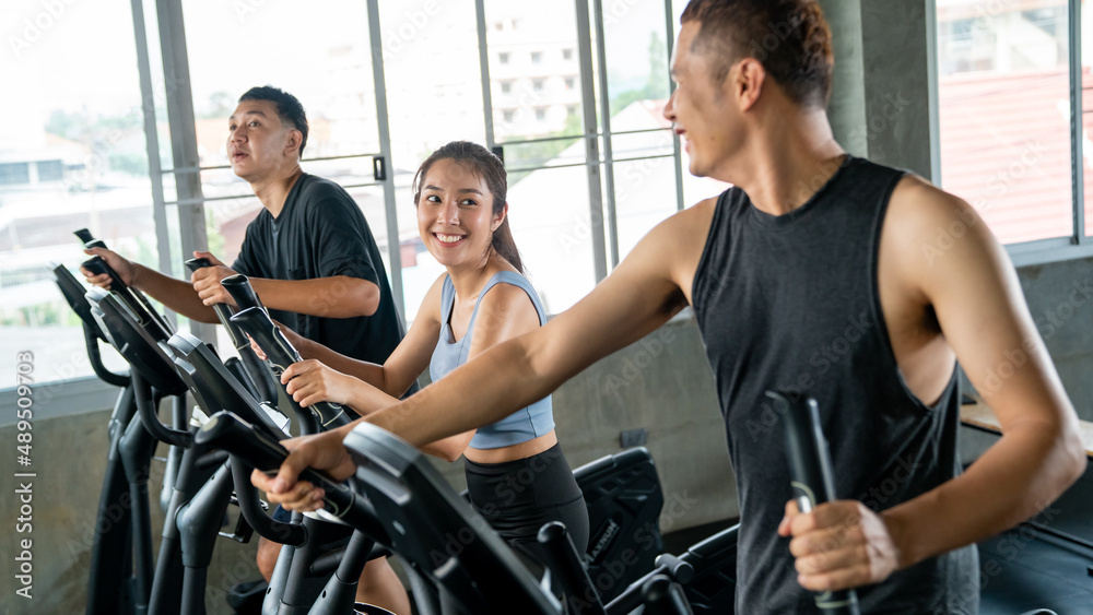 Healthy Asian athletic man and woman in sportswear workout exercise on cycling machine together at fitness gym. Wellness male and female do sport training at sport club. Health care motivation concept