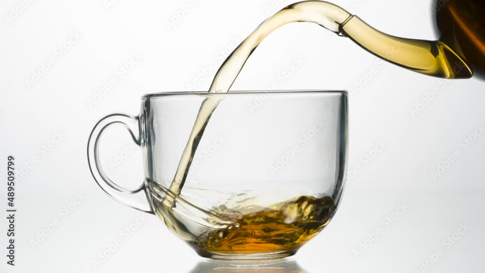 Fragrant Tea is Poured Into a Cup. A stream of strong tea flows out of the glass spout of the teapot into a glass cup on a bright white background