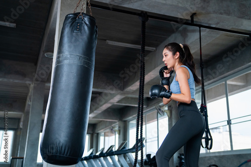 4K Strong Asian athletic woman in sportswear wearing boxing gloves do workout exercise punching boxing bag at fitness gym. Healthy fit and firm female do sport training and bodybuilding at sport club.