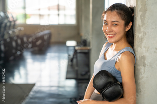 Portrait of Asian athletic woman in sportswear and boxing gloves do workout exercise punching boxing bag at fitness gym. Healthy fit and firm female do sport training and bodybuilding at sport club photo