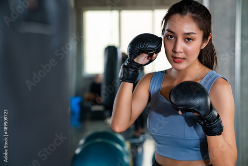 Portrait of Asian athletic woman in sportswear and boxing gloves do workout exercise punching boxing bag at fitness gym. Healthy fit and firm female do sport training and bodybuilding at sport club © CandyRetriever 