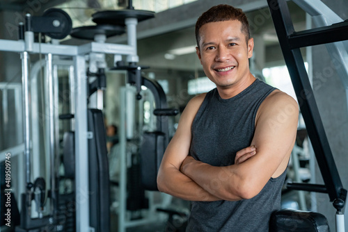 Portrait of Smiling Asian athletic man in sportswear workout exercise with exercise machine at fitness gym. Healthy wellness male do sport training at sport club. Health care motivation concept