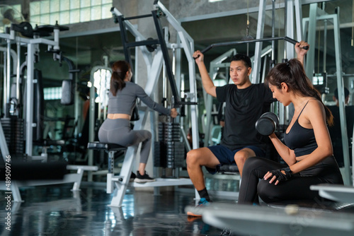 Healthy Asian athletic man and woman in sportswear workout exercise weight lifting at fitness gym. Male and female do body building weight training at sport club. Health care motivation concept