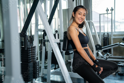 Portrait of Smiling Asian athletic woman in sportswear workout exercise with exercise machine at fitness gym. Healthy wellness female do sport training at sport club. Health care motivation concept