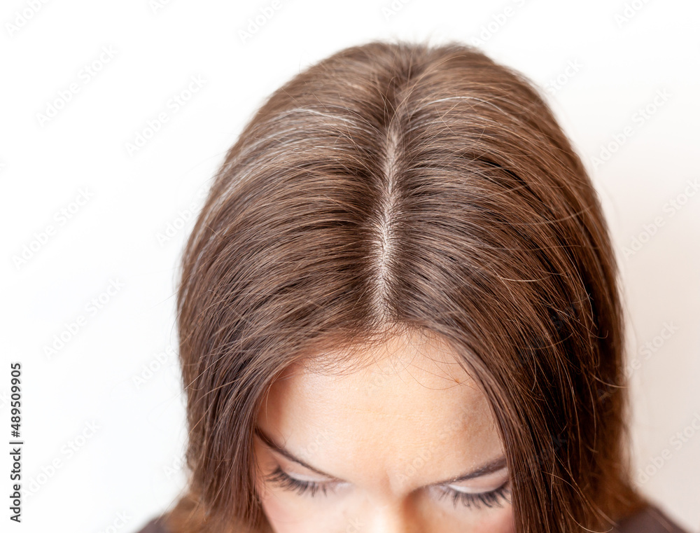 A woman's head with a parting of gray hair that has grown roots due to quarantine. Brown hair on a woman's head close-up. Hair regrowth A woman's head with a parting of gray hair that has grown roots due to quarantine. Brown hair on a woman's head close-up. Hair regrowth