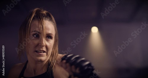 A Strong, Fierce Kickboxing Woman Training On A Punching Bag In An MMA Gym. Shot In A Crossfit Boxing Gym With Low Key Lighting And A Scattering Of Haze. Captured On Red Digital Cinema Camera 