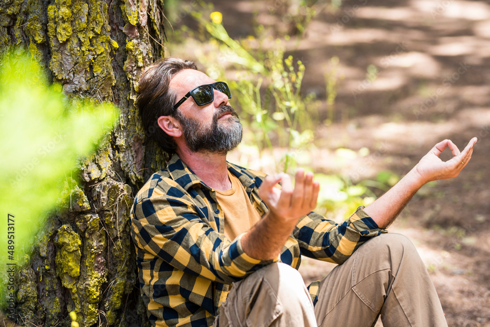 Adult hipster bearded man meditate and have relax outdoor leisure activity in the forest woods sitting against a tree trunk and enjoying nature feeling and love around. Male people enjoy life