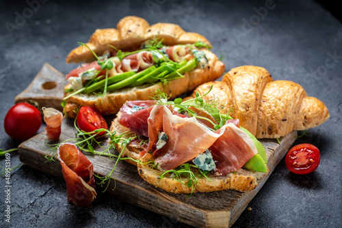 Variety of aperitifs Croissant sandwiches with jamon ham serrano paleta iberica, blue cheese, avocado, microgin on blue background. Delicious snack, appetizers, tapas photo