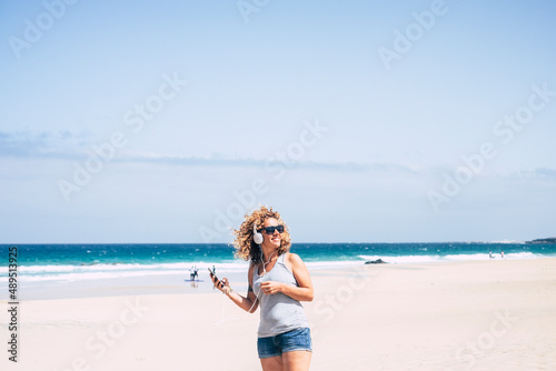Happy female tourist enjoy leisure outdoors at the beach listening music from mobile phone and headset amiling and enjoying summer holiday vacation travel lifestyle. Cheerful pretty woman
