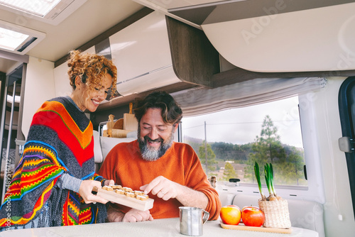 Couple of people enjoy leisure indoor in a camper camping car. Adult man and woman smile and have fun during travel vacation or vanlife. Renting rv van or living vanlife style. Modern alternative home