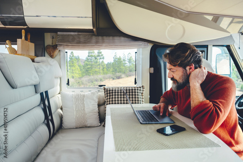 Young modern adult man work on laptop computer in remote working and digital job lifestyle inside a modern and connected camper van with nature woods view outside the window. Freedom lifestyle people