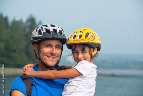 Portrait of a smiling man with her daughter, wearing helmets and ready for riding bicycles, embracing each other.