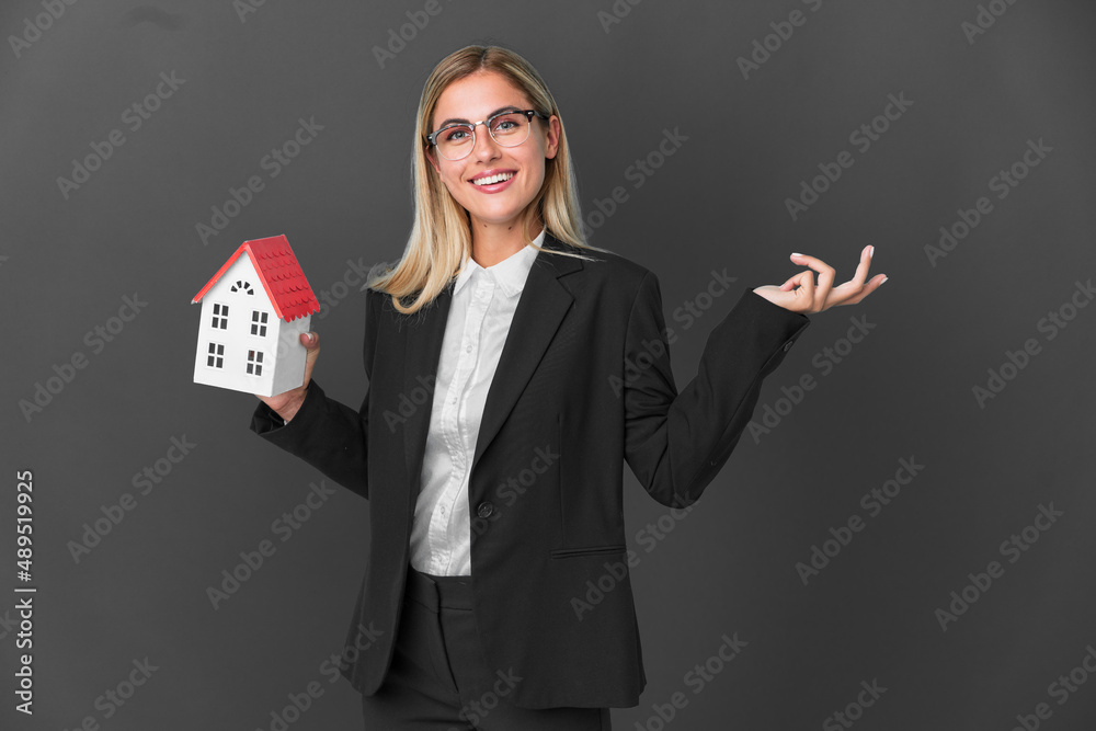 Blonde Uruguayan girl holding a house toy isolated on black background extending hands to the side for inviting to come Blonde Uruguayan girl holding a house toy isolated on black background extending hands to the side for inviting to come