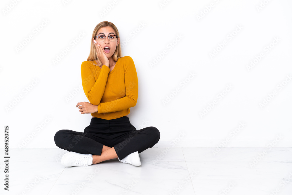 Blonde Uruguayan girl sitting on the floor surprised and shocked while looking right