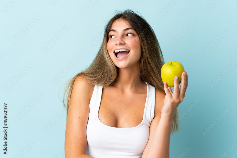 Young caucasian woman isolated on blue background with an apple and happy Young caucasian woman isolated on blue background with an apple and happy