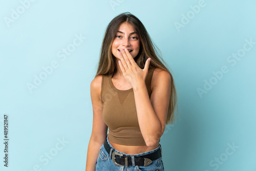 Young caucasian woman isolated on blue background happy and smiling covering mouth with hand