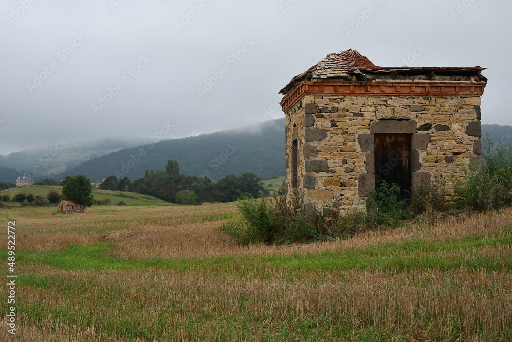 Petite maison de vigneron en pierre dans un  champ avec à l’arrière un banc de brouillard descendant de la montagne 