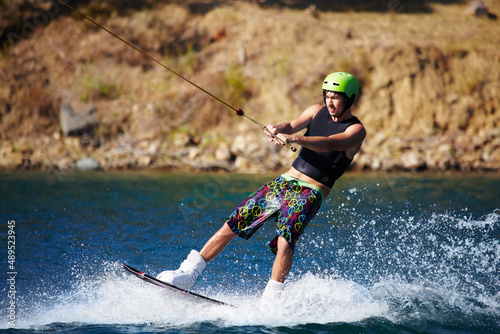 A young man wearing a helmut and lifejacket wakeboarding on a lake. A young man wearing a helmet and lifejacket wakeboarding on a lake.